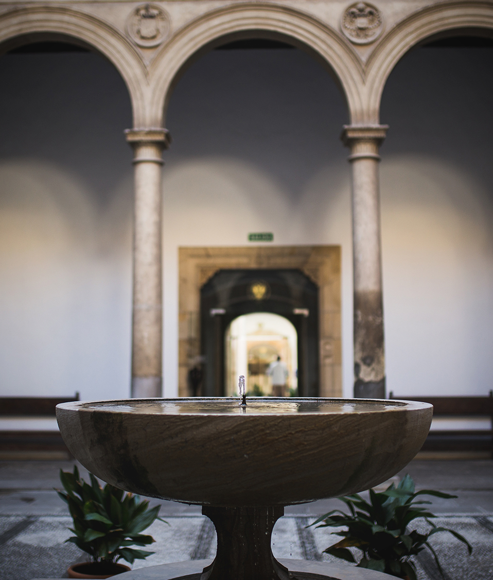 Fuente ornamental central de uno de los patios del Hospital Real con los arcos de columnas al fondo
