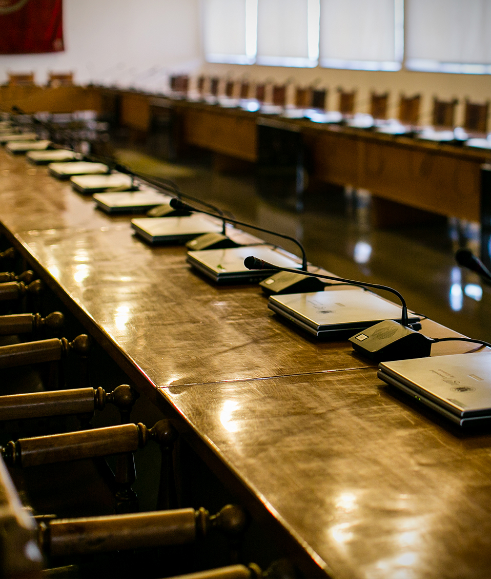Imagen de la Sala de Convalecientes del Hospital Real de la Universidad de Granada. Espacio de reunión donde hay disponibles asientos, micrófonos y ordenadores para cada interlocutor. En la imagen se encuentran mesas y asientos de estilo clásico